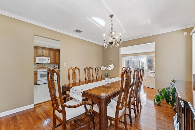 dining space featuring crown molding, visible vents, an inviting chandelier, light wood-type flooring, and baseboards