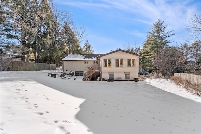 snow covered rear of property featuring fence, a wooden deck, and stairs