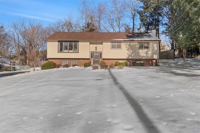 split foyer home featuring a chimney, fence, and brick siding