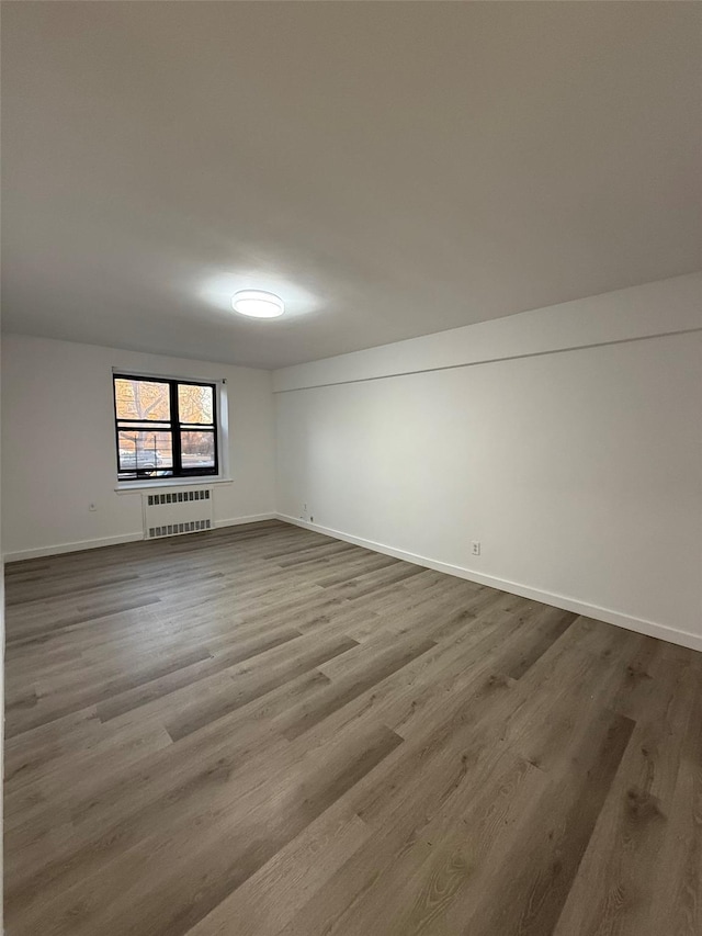 empty room with baseboards, radiator heating unit, and wood finished floors