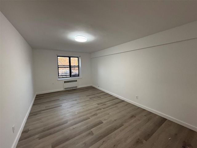 spare room with radiator, baseboards, and wood finished floors