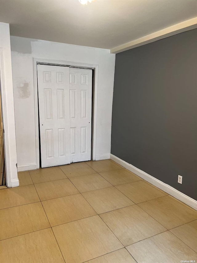 unfurnished bedroom featuring light tile patterned floors, baseboards, and a closet