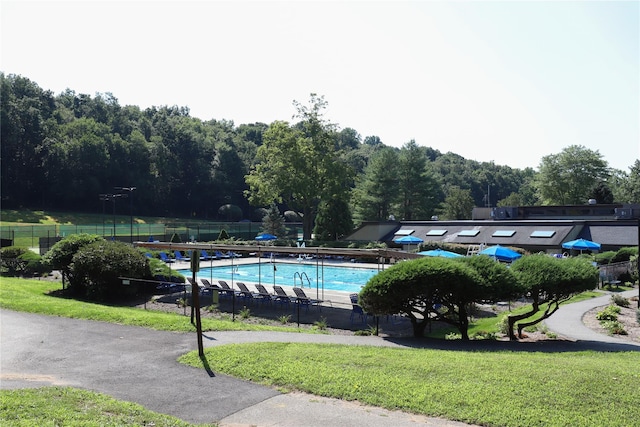 community pool featuring a yard, fence, and a view of trees