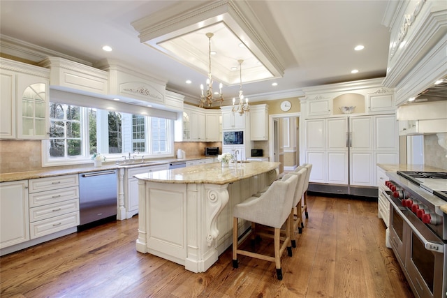 kitchen with stainless steel appliances, ornamental molding, a raised ceiling, and white cabinetry