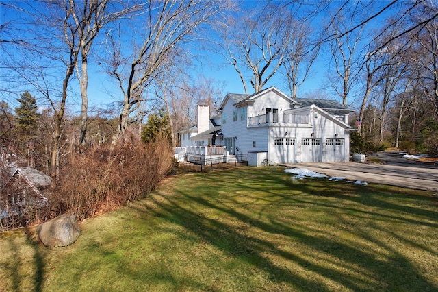 view of property exterior with driveway, a lawn, a chimney, and a balcony