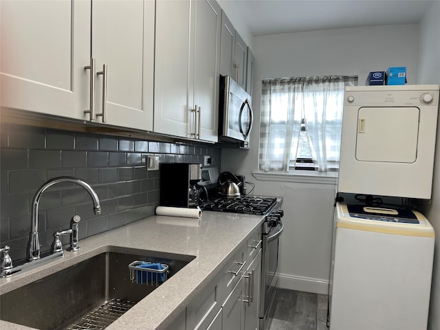 kitchen with wood finished floors, a sink, appliances with stainless steel finishes, decorative backsplash, and stacked washer and clothes dryer