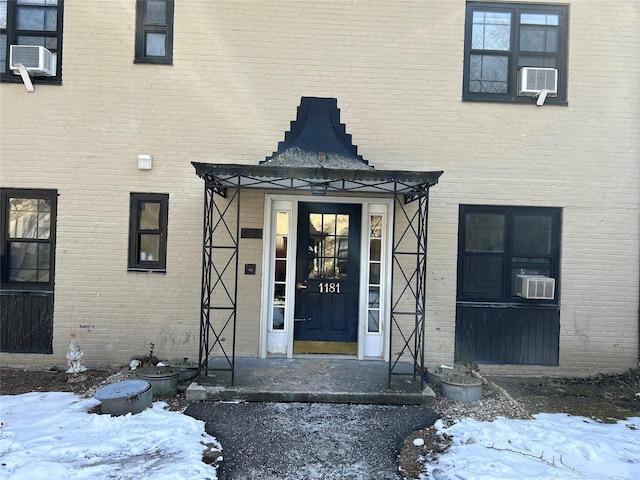 snow covered property entrance with brick siding and cooling unit