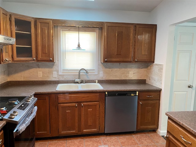 kitchen with brown cabinetry, dark countertops, glass insert cabinets, stainless steel appliances, and a sink