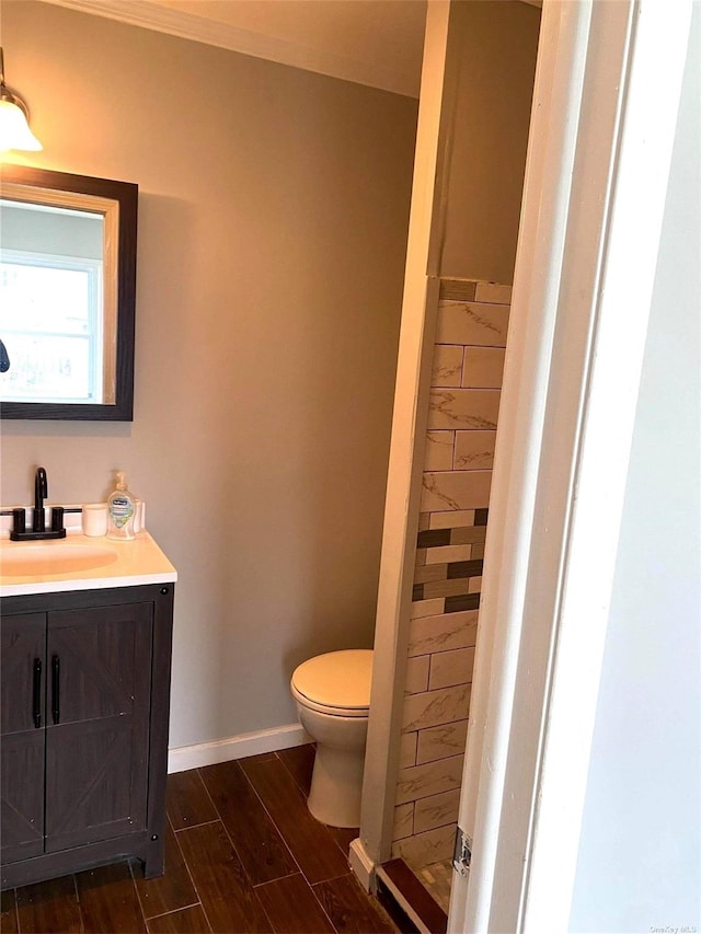 bathroom with toilet, wood finished floors, vanity, baseboards, and walk in shower