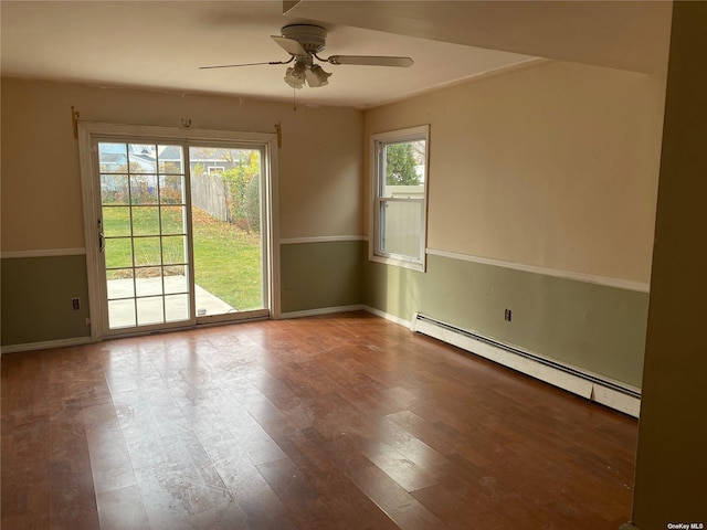 spare room featuring a ceiling fan, a wealth of natural light, baseboard heating, and wood finished floors