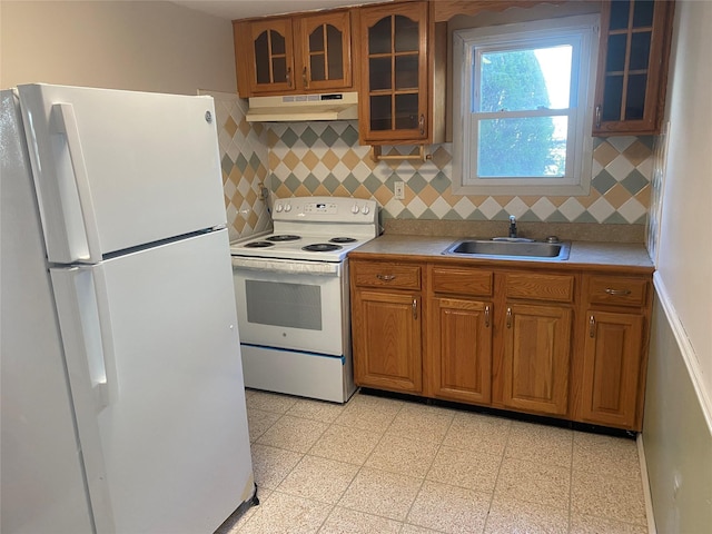 kitchen with white appliances, glass insert cabinets, light countertops, under cabinet range hood, and a sink