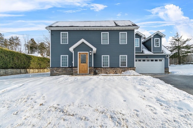 colonial-style house featuring stone siding, aphalt driveway, and an attached garage