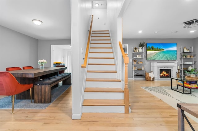 stairway featuring a lit fireplace, wood finished floors, and recessed lighting