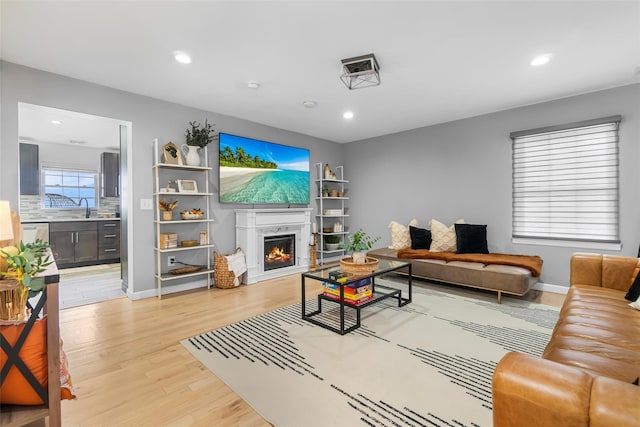 living area featuring recessed lighting, a warm lit fireplace, light wood-style flooring, and baseboards