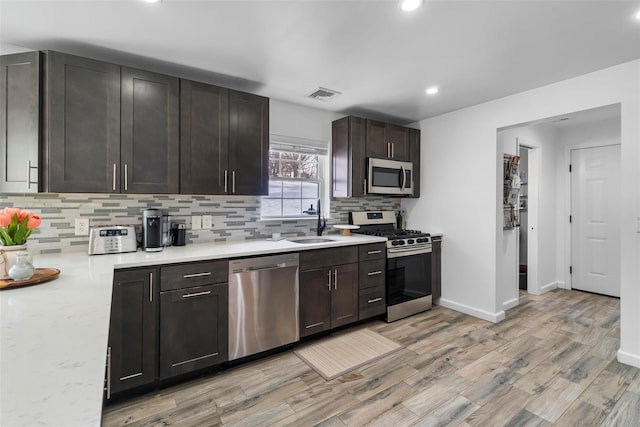 kitchen with visible vents, light wood-style flooring, appliances with stainless steel finishes, a sink, and dark brown cabinets