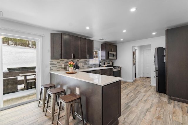 kitchen with a peninsula, light countertops, appliances with stainless steel finishes, tasteful backsplash, and a kitchen bar