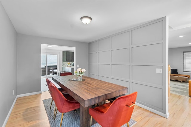 dining area featuring light wood-type flooring, a decorative wall, and baseboards