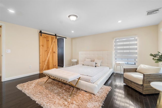 bedroom with a barn door, visible vents, dark wood finished floors, and baseboards