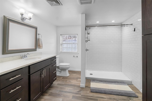 bathroom featuring toilet, wood finished floors, vanity, visible vents, and a stall shower