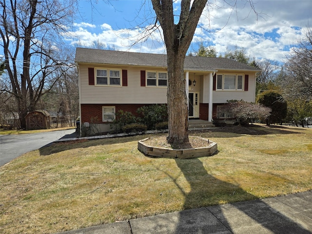 raised ranch featuring brick siding, a front yard, and an outdoor structure