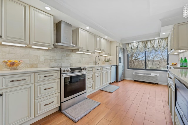 kitchen with light wood finished floors, light countertops, decorative backsplash, appliances with stainless steel finishes, and wall chimney range hood