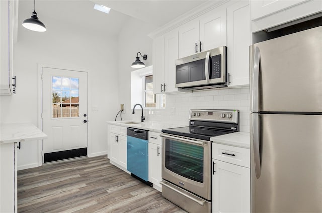 kitchen featuring decorative backsplash, white cabinets, stainless steel appliances, light wood-type flooring, and a sink