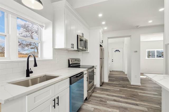 kitchen with stainless steel appliances, backsplash, white cabinetry, a sink, and wood finished floors