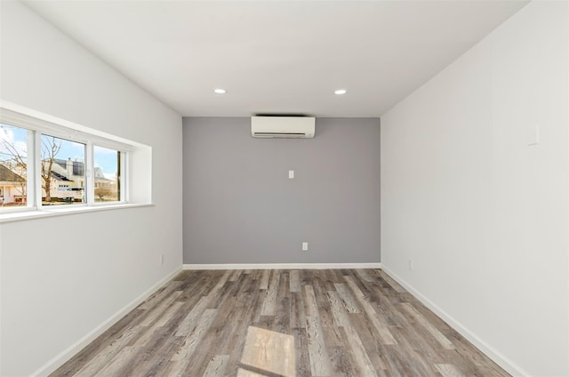 unfurnished room featuring a wall unit AC, light wood-style flooring, baseboards, and recessed lighting