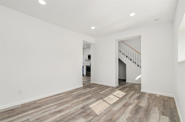 unfurnished living room featuring light wood finished floors, stairs, baseboards, and recessed lighting