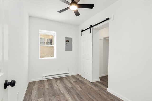 unfurnished bedroom featuring a barn door, a baseboard radiator, wood finished floors, baseboards, and electric panel