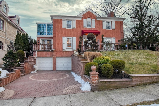 view of front facade with a balcony, an attached garage, a chimney, decorative driveway, and brick siding