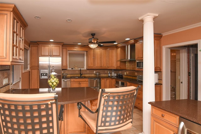 kitchen featuring a sink, tasteful backsplash, stainless steel appliances, wall chimney range hood, and ornate columns