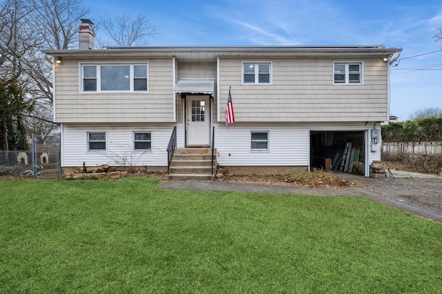 bi-level home with an attached garage, aphalt driveway, fence, and a front lawn