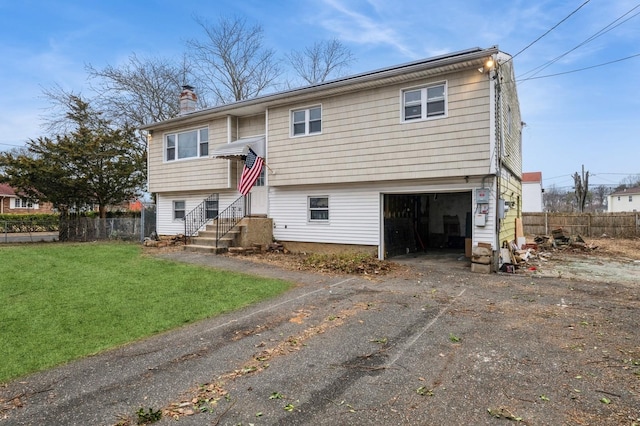 bi-level home with aphalt driveway, a garage, fence, a chimney, and a front yard