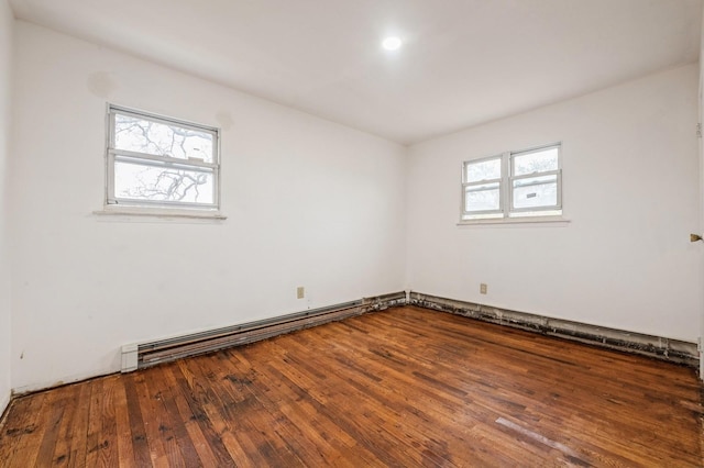 spare room featuring a baseboard heating unit, a healthy amount of sunlight, and hardwood / wood-style flooring