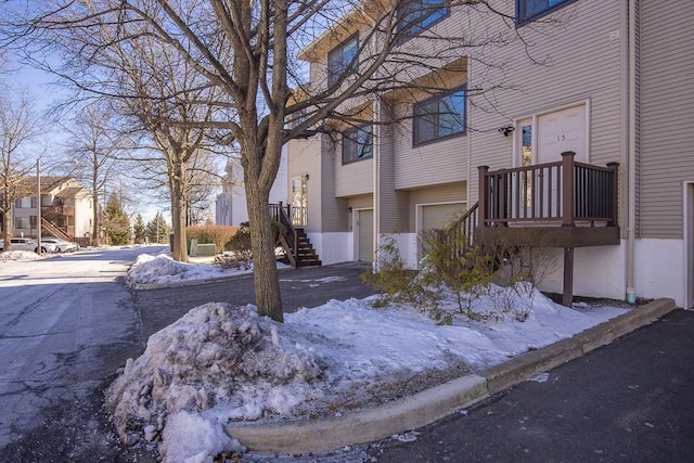 snow covered property with a garage, driveway, and stairs