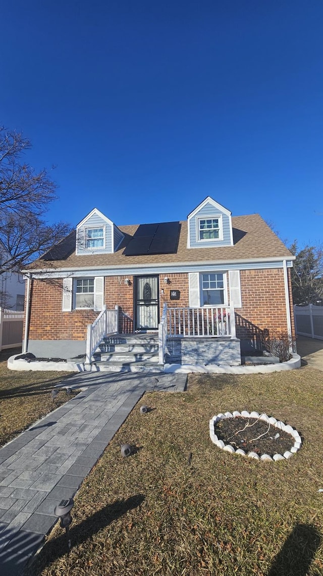 view of front of home featuring a porch, solar panels, brick siding, fence, and a front lawn