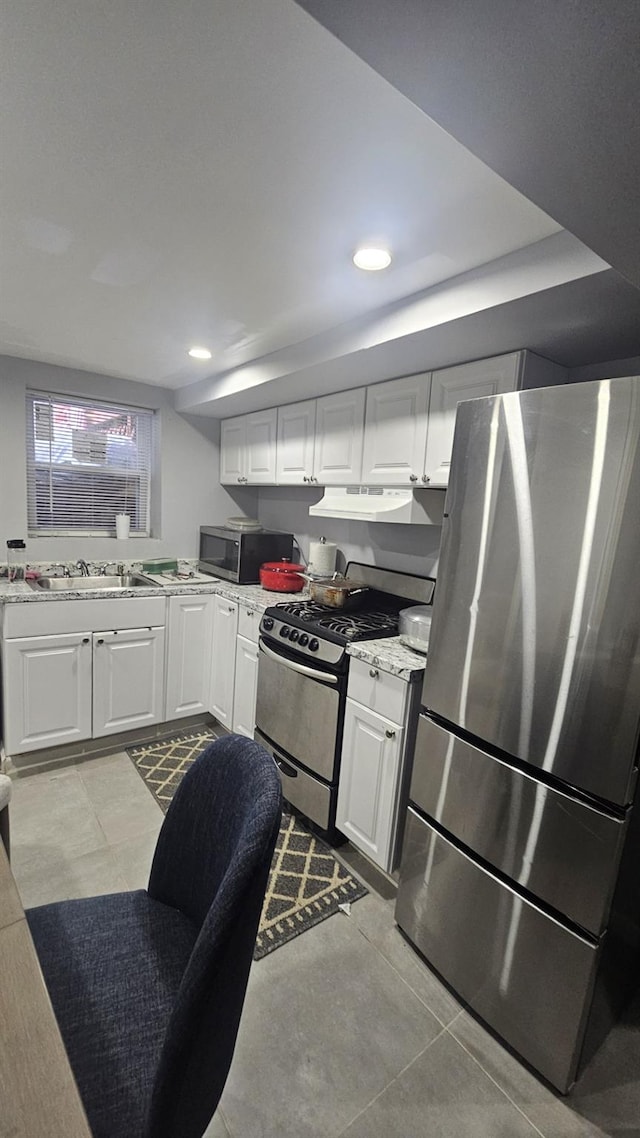 kitchen featuring light stone counters, under cabinet range hood, a sink, white cabinetry, and appliances with stainless steel finishes