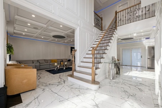 stairs featuring crown molding, marble finish floor, coffered ceiling, and a decorative wall