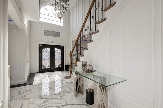 entrance foyer featuring stairway, marble finish floor, a high ceiling, french doors, and a decorative wall