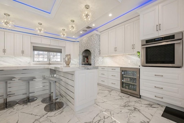 kitchen featuring beverage cooler, white cabinets, a kitchen breakfast bar, light countertops, and stainless steel oven