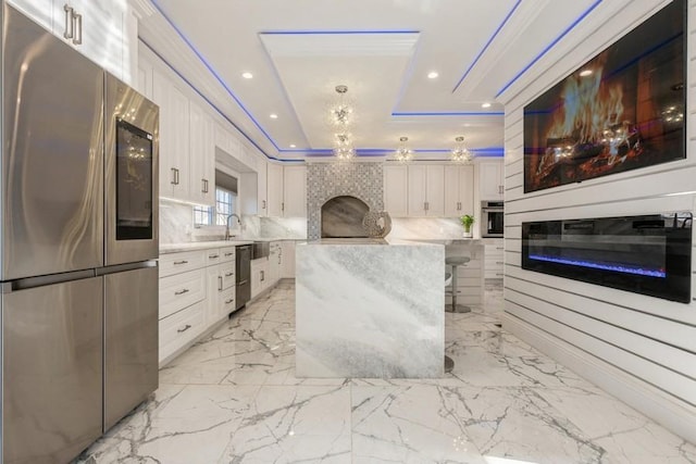 kitchen featuring white cabinets, a tray ceiling, stainless steel appliances, and a glass covered fireplace