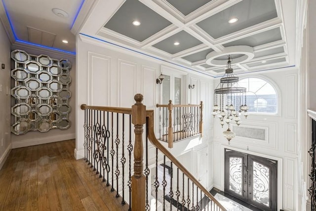 hallway featuring coffered ceiling, french doors, wood finished floors, crown molding, and an upstairs landing