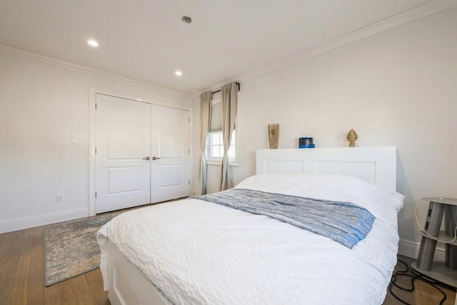 bedroom featuring dark wood-type flooring, a closet, crown molding, and baseboards