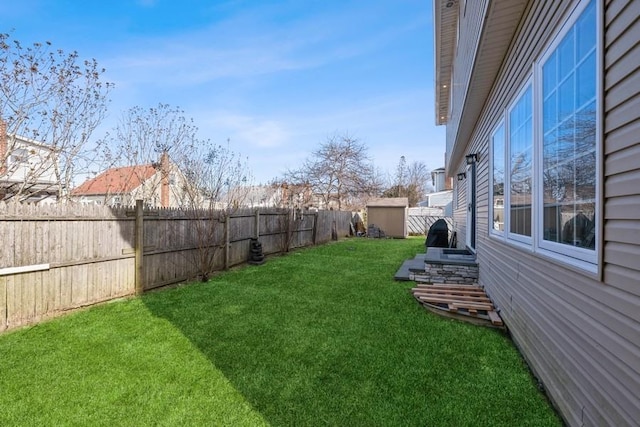 view of yard with a storage shed, a fenced backyard, and an outbuilding