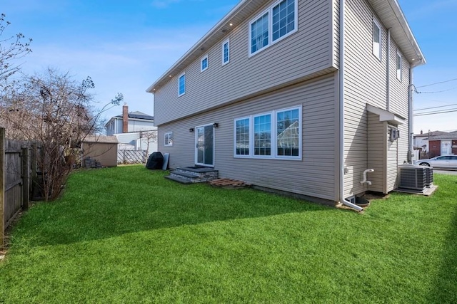 back of property with central air condition unit, a lawn, and fence