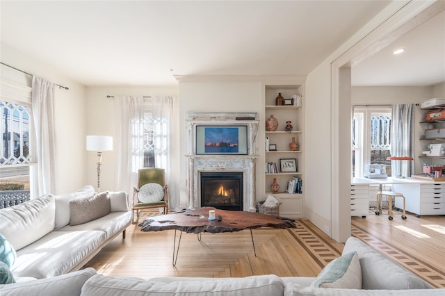 living room with built in shelves, a glass covered fireplace, and light wood-style floors