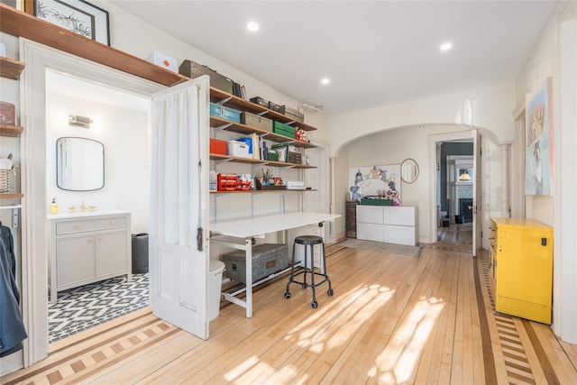 interior space with light wood finished floors, arched walkways, a sink, and recessed lighting