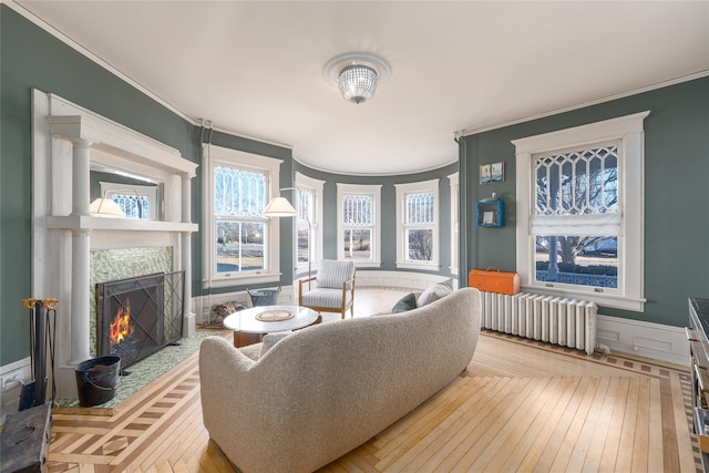 living area with radiator heating unit, a tile fireplace, light wood-style flooring, and crown molding