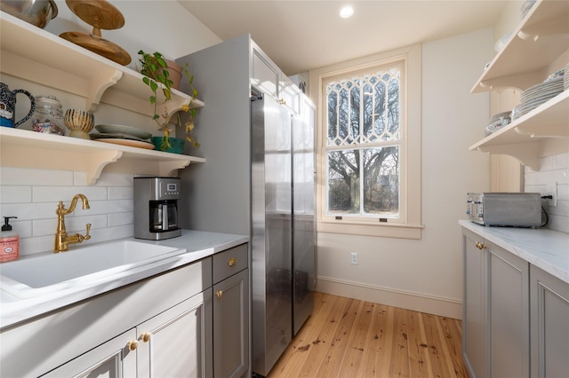 kitchen with open shelves, light wood-style flooring, decorative backsplash, a sink, and baseboards